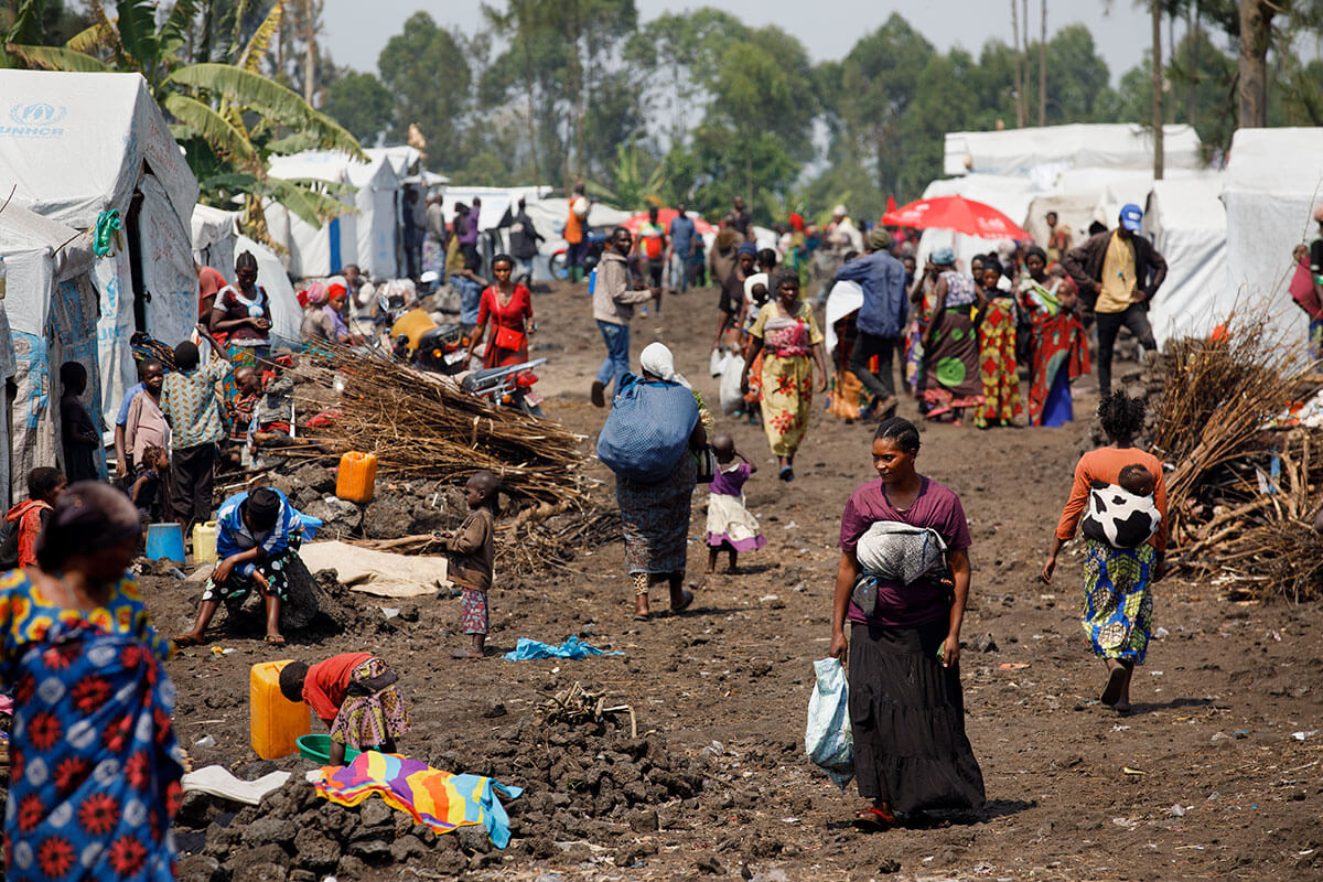 In the Democratic Republic of Congo, a woman walks through Rusayo camp for internally displaced people in August 2023. Located outside of Goma, the camp emerged as a shelter for people taking refuge from violence and, according to the World Food Programme, has grown from housing 45,000 people in January 2023 to 95,000 people by February 2024. Photo: UN Women/Ryan Brown.