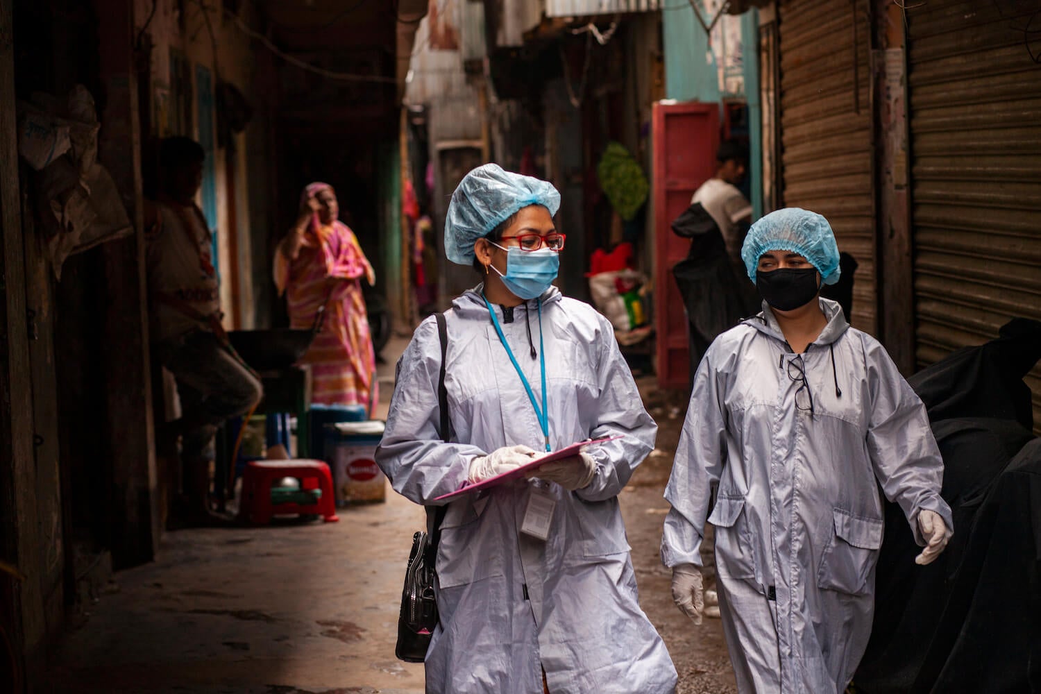 Two women in full PPE walking in the street with a clipboard.