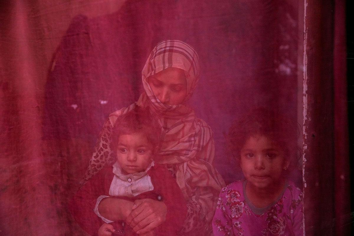 Now unemployed, a woman sits at home with her two daughters. Photo: UN Women/Sayed Habib Bidell.