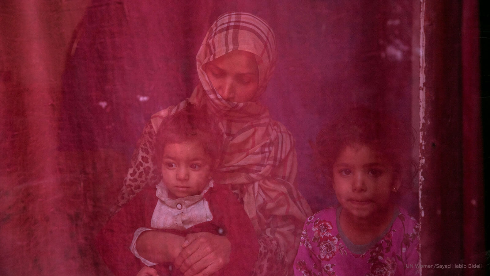 Now unemployed, a woman sits at home with her two daughters. Photo: UN Women/Sayed Habib Bidell.