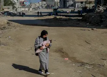 Salma, a 29-year-old, carries her infant while walking on Rashid Street, west of Gaza City, on 11 January 2024.