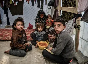 A family is seen sitting around a bowl of beans in their tent in Rafah, in the south of the Gaza Strip. 