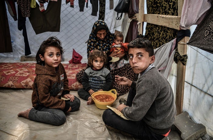 A family is seen sitting around a bowl of beans in their tent in Rafah, in the south of the Gaza Strip. 